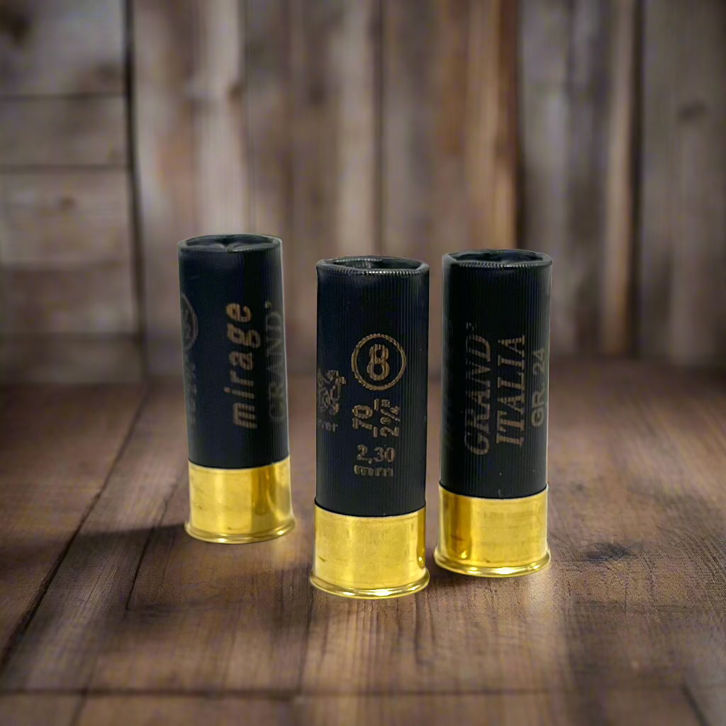 Three black fake 12GA Clever Mirage dummy rounds standing upright on a rustic wooden table with a wood panel background.