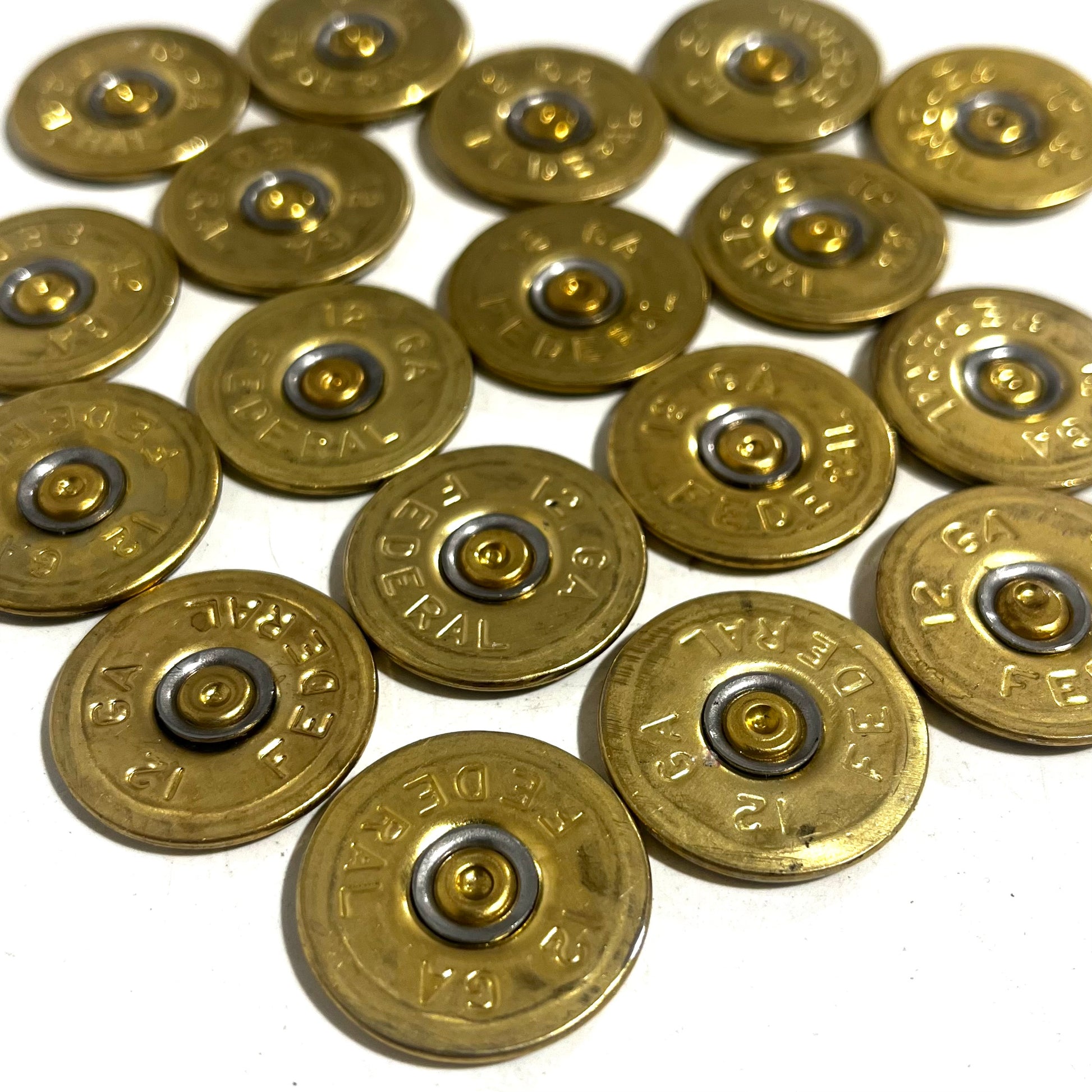 18 round brass 12 gauge Federal headstamp slices arranged in a cluster on a white background