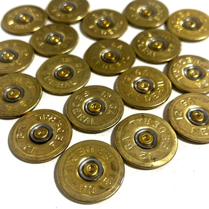 18 round brass 12 gauge Federal headstamp slices arranged in a cluster on a white background