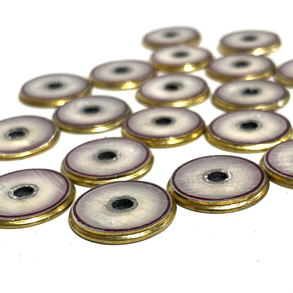 Round brass 12 gauge shotgun shell slices with white and burgundy enamel-lined centers and a hole punched through the middle