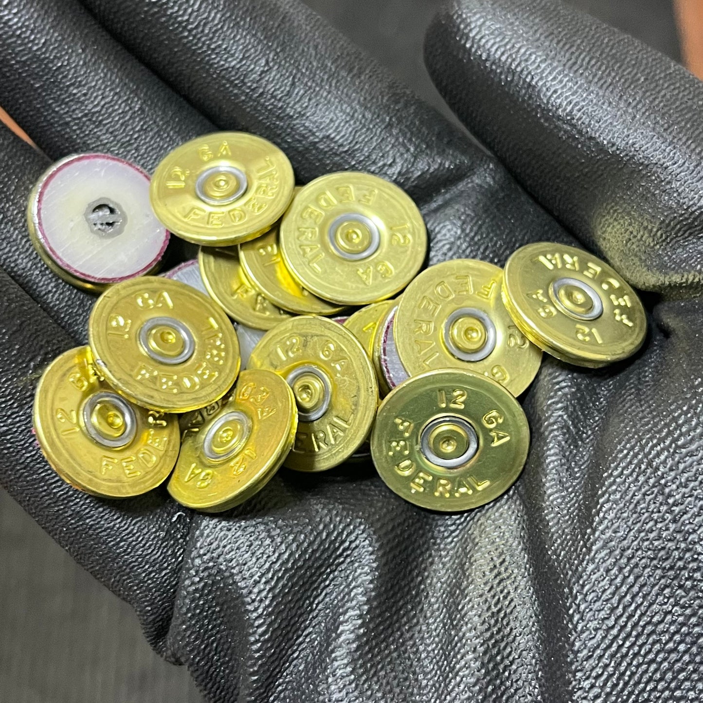 Round brass 12 gauge Federal headstamp slices held in a gloved hand
