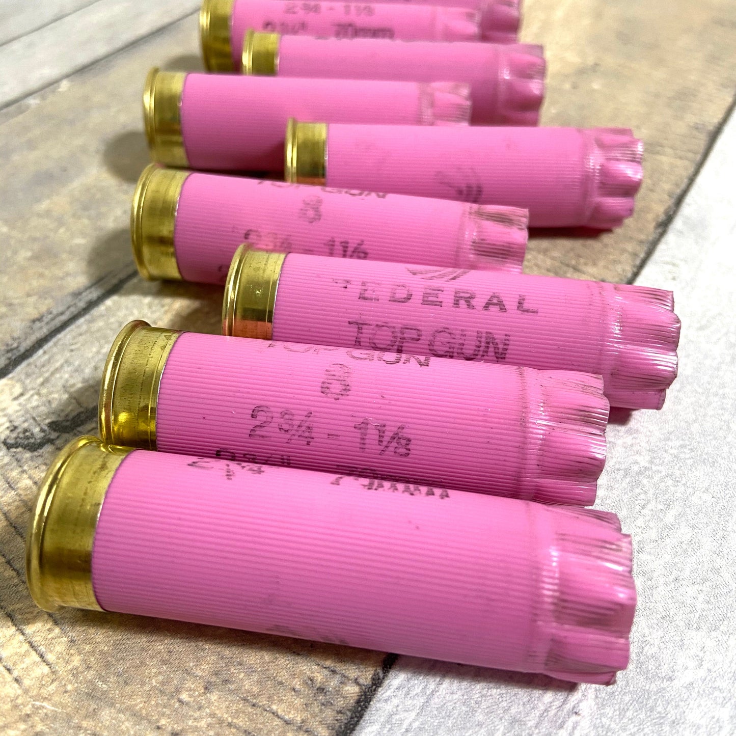 Row of pink Federal Top Gun 12 gauge shotgun shell hulls on a wood plank surface showing "2 3/4-1 1/8" markings