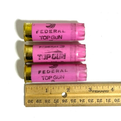Three pink Federal Top Gun 12 gauge shotgun shell hulls stacked beside a wooden ruler for scale