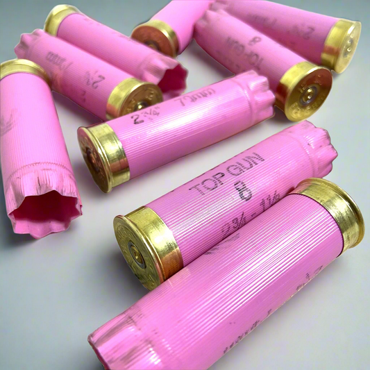 Seven pink Federal Top Gun 12 gauge shotgun shell hulls scattered on a light gray surface, some with open crimped mouths