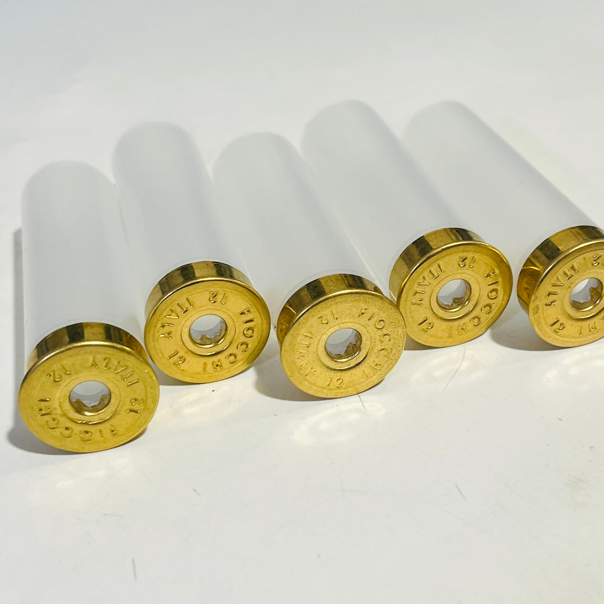 Row of five clear 12 gauge Fiocchi hulls, never fired, with FIOCCHI 12 ITALY headstamps and empty primer pockets for Christmas light strings