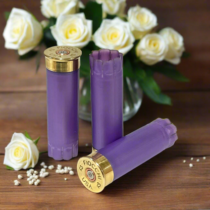 Three light purple Fiocchi unmarked once-fired 12-gauge hulls with gold bases, arranged near white roses and pearls