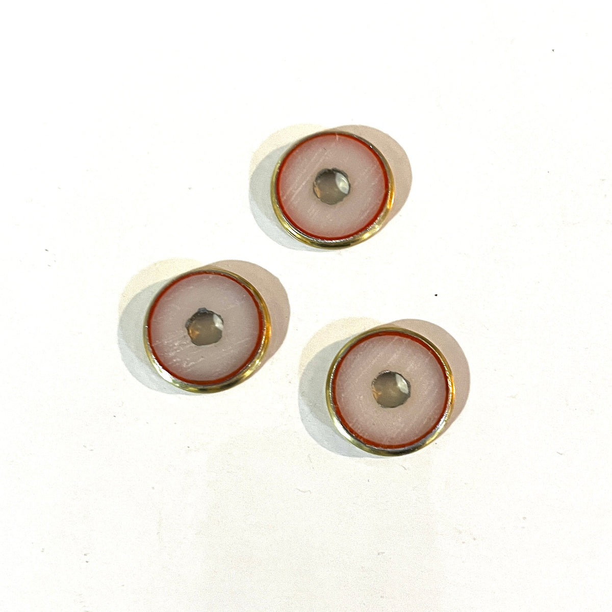 3 round brass 12 gauge shotgun shell slices with white and red enamel-lined centers on a white background