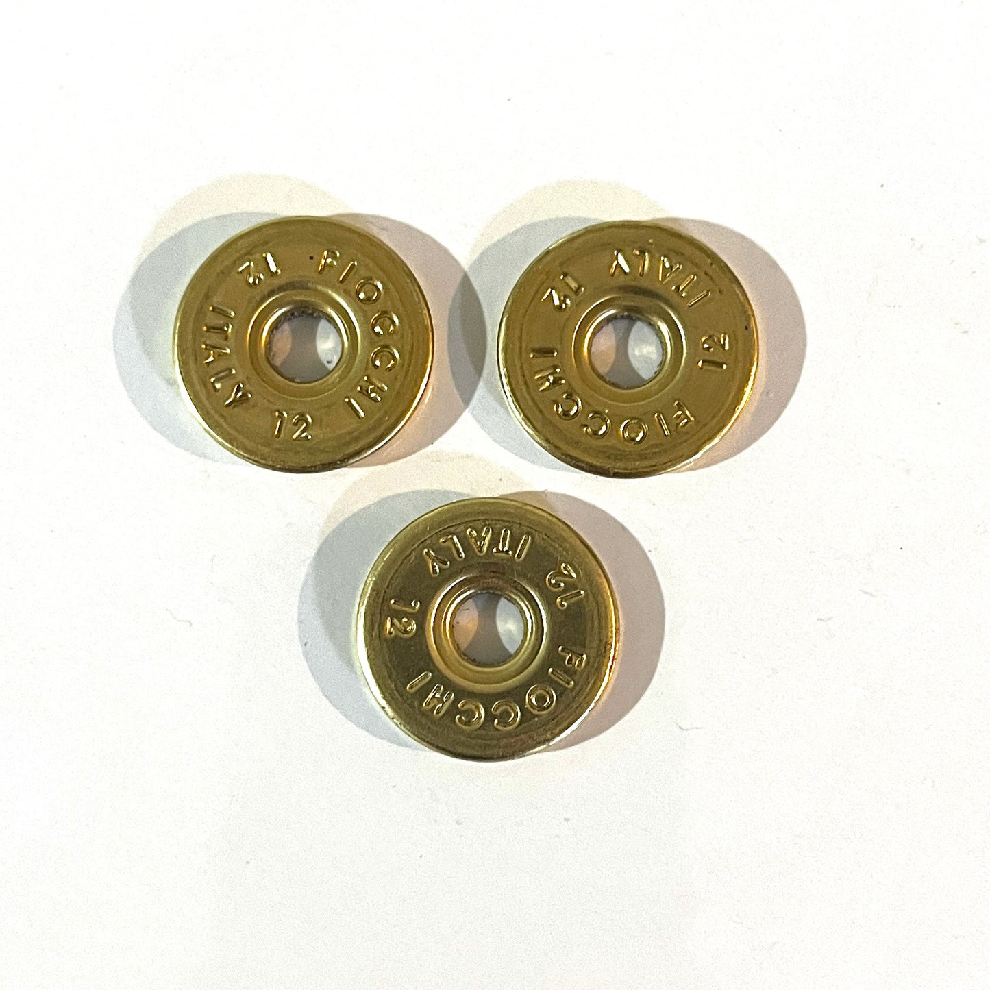 3 round brass 12 gauge Fiocchi Italy headstamp slices on a white background