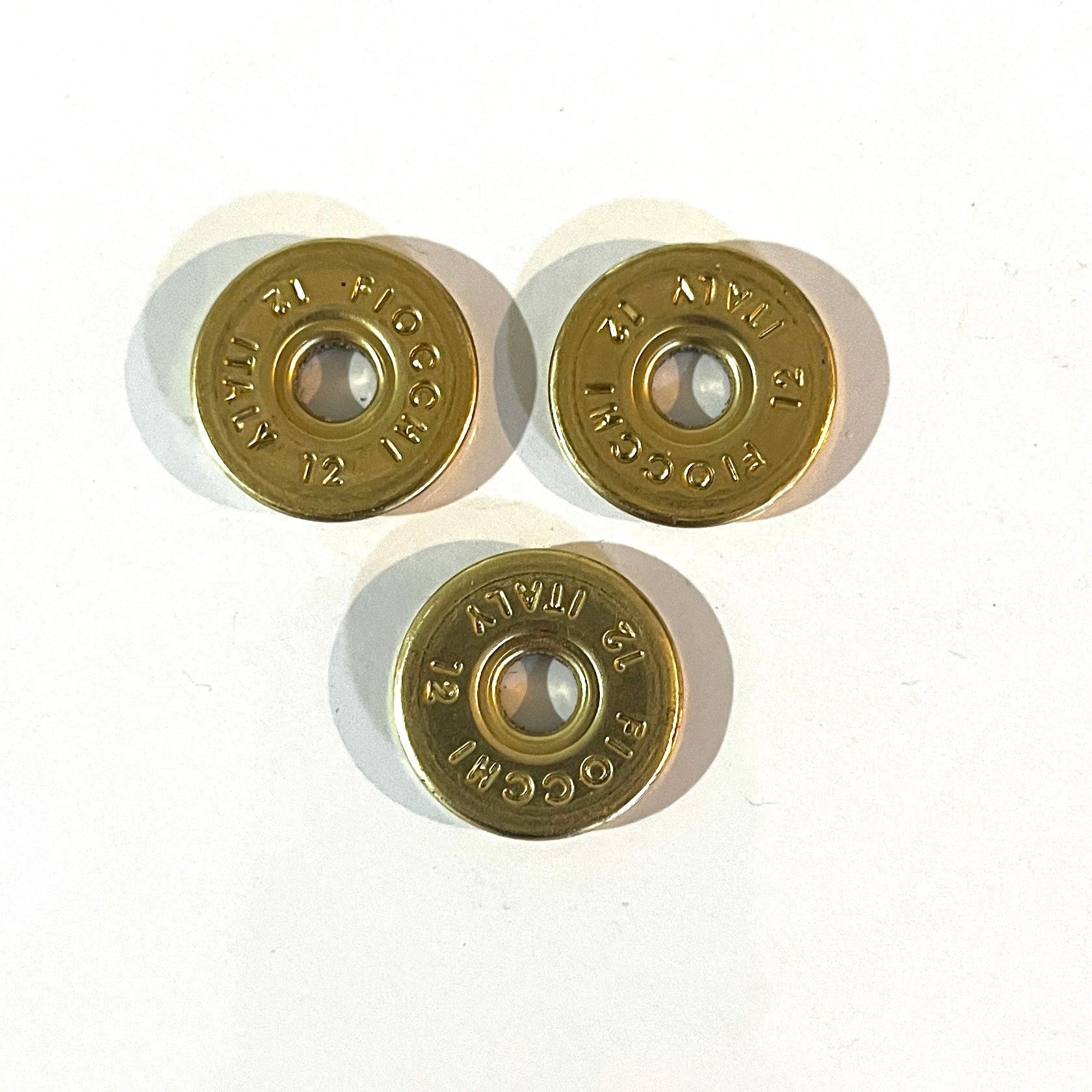 3 round brass 12 gauge Fiocchi Italy headstamp slices on a white background