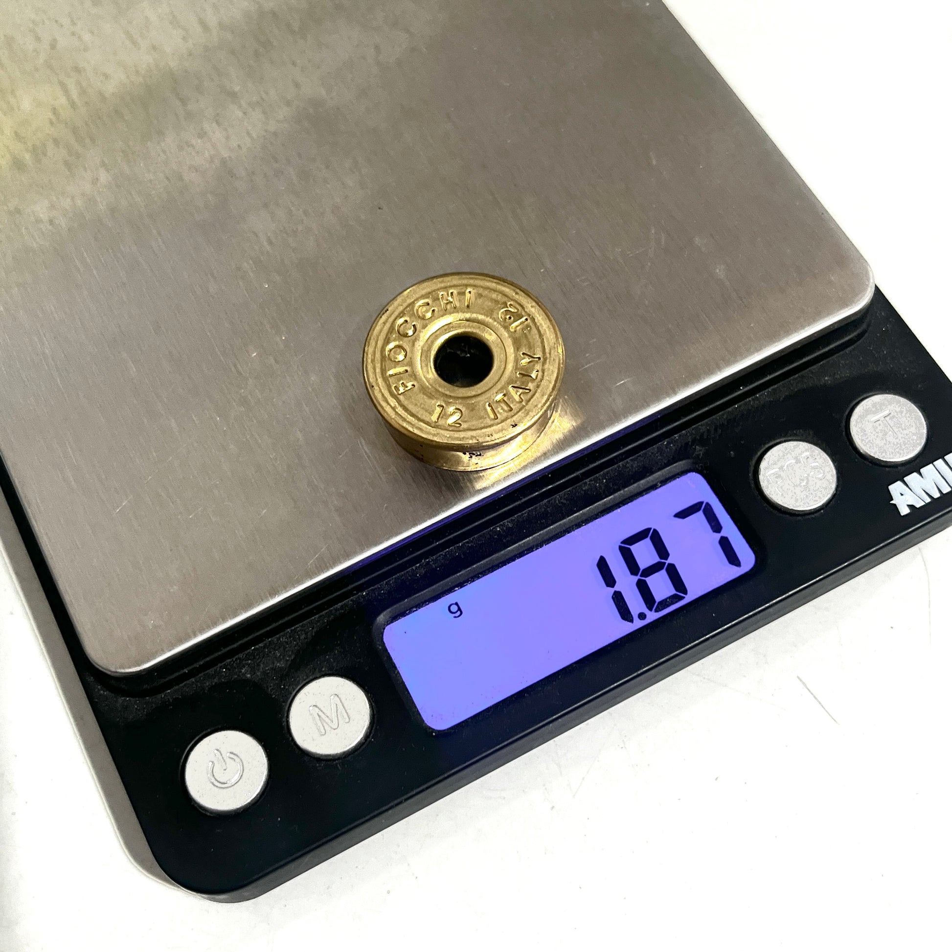 Gold Fiocchi 12 gauge deprimed headstamp on a digital scale displaying a weight of 1.87 grams.