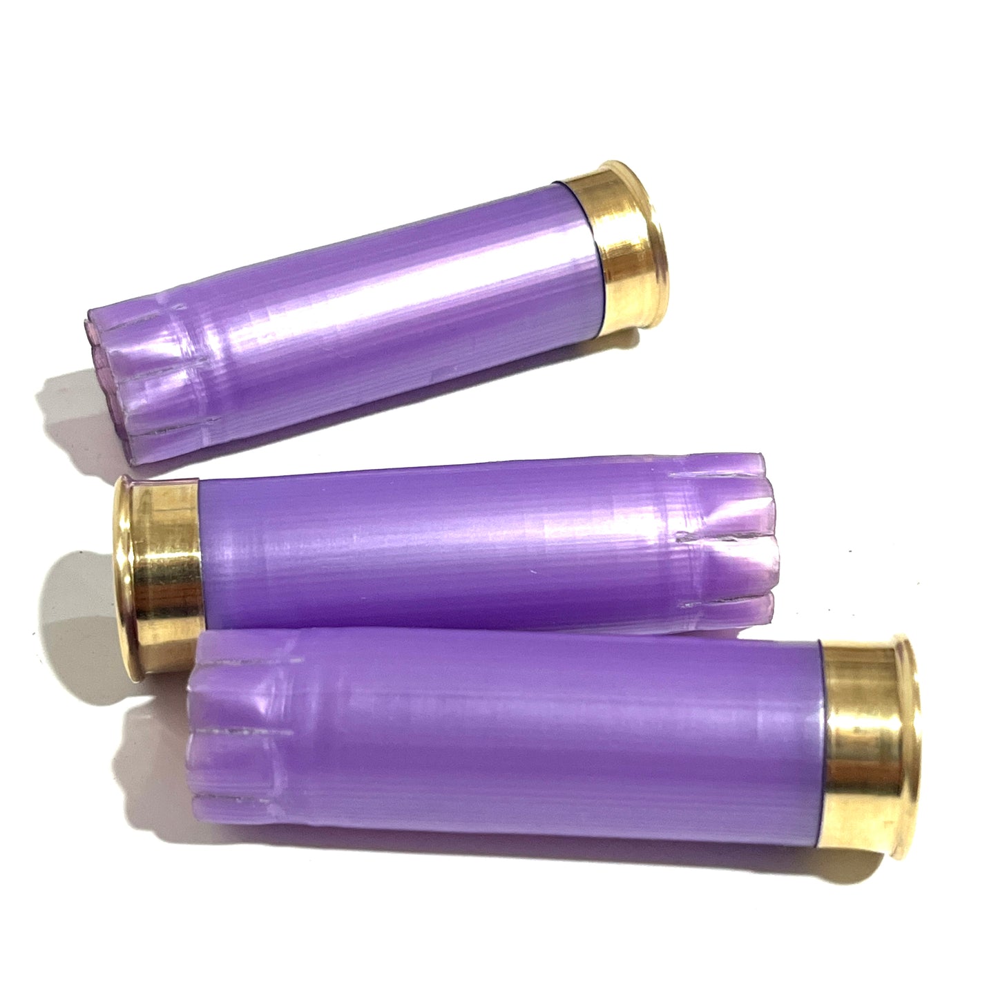 Three light purple spent casings lying on their sides with polished gold bases and crimped ends on a white background for boutonnieres