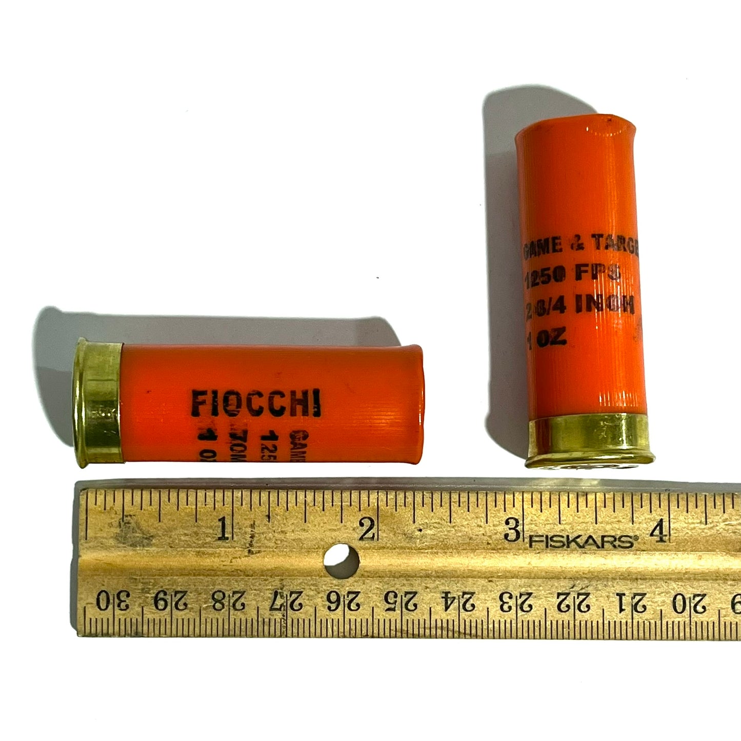 Two spent orange Fiocchi hulls beside a wooden ruler for size reference.
