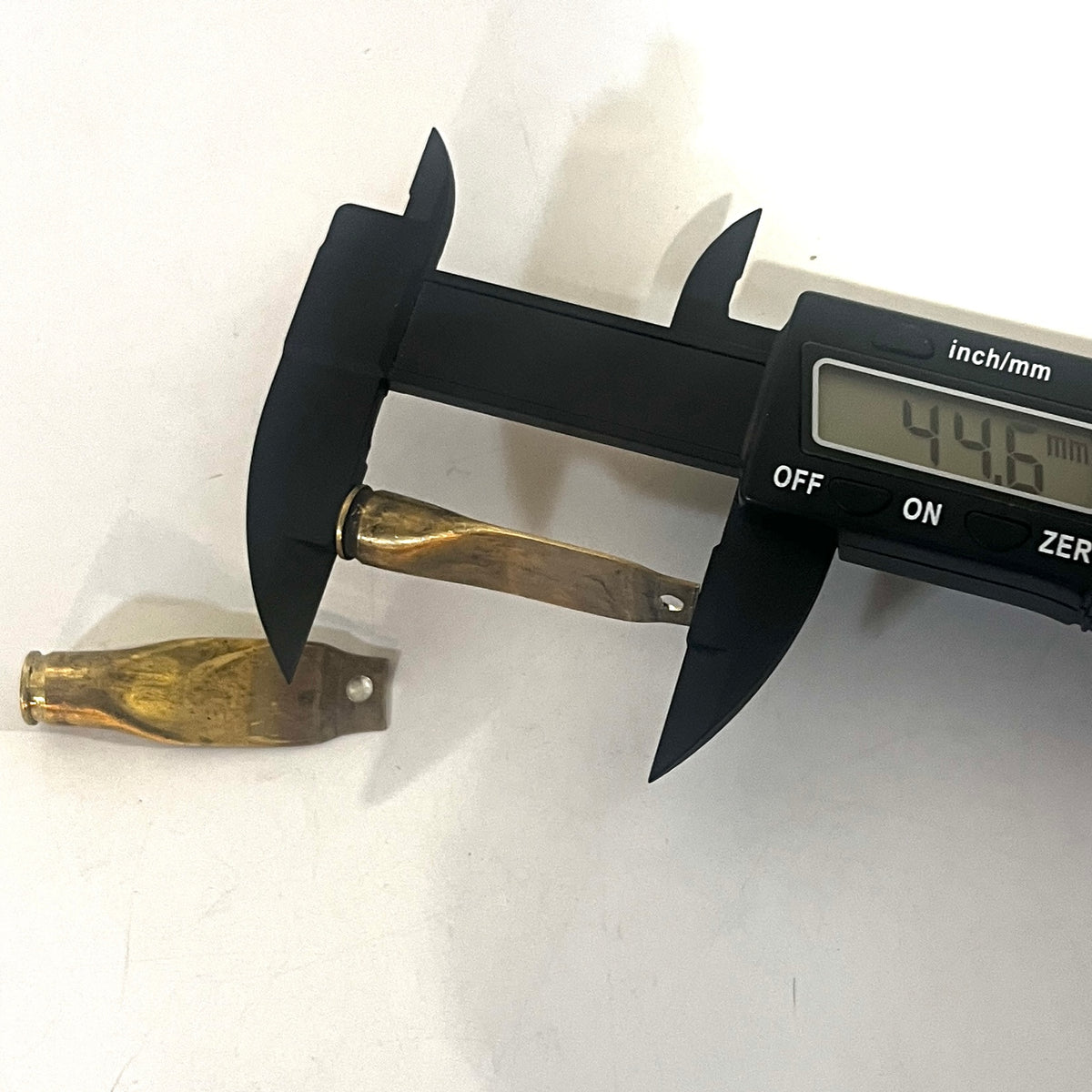 Digital caliper measuring the length of a flattened brass casing showing 44.6 mm with another casing beside it