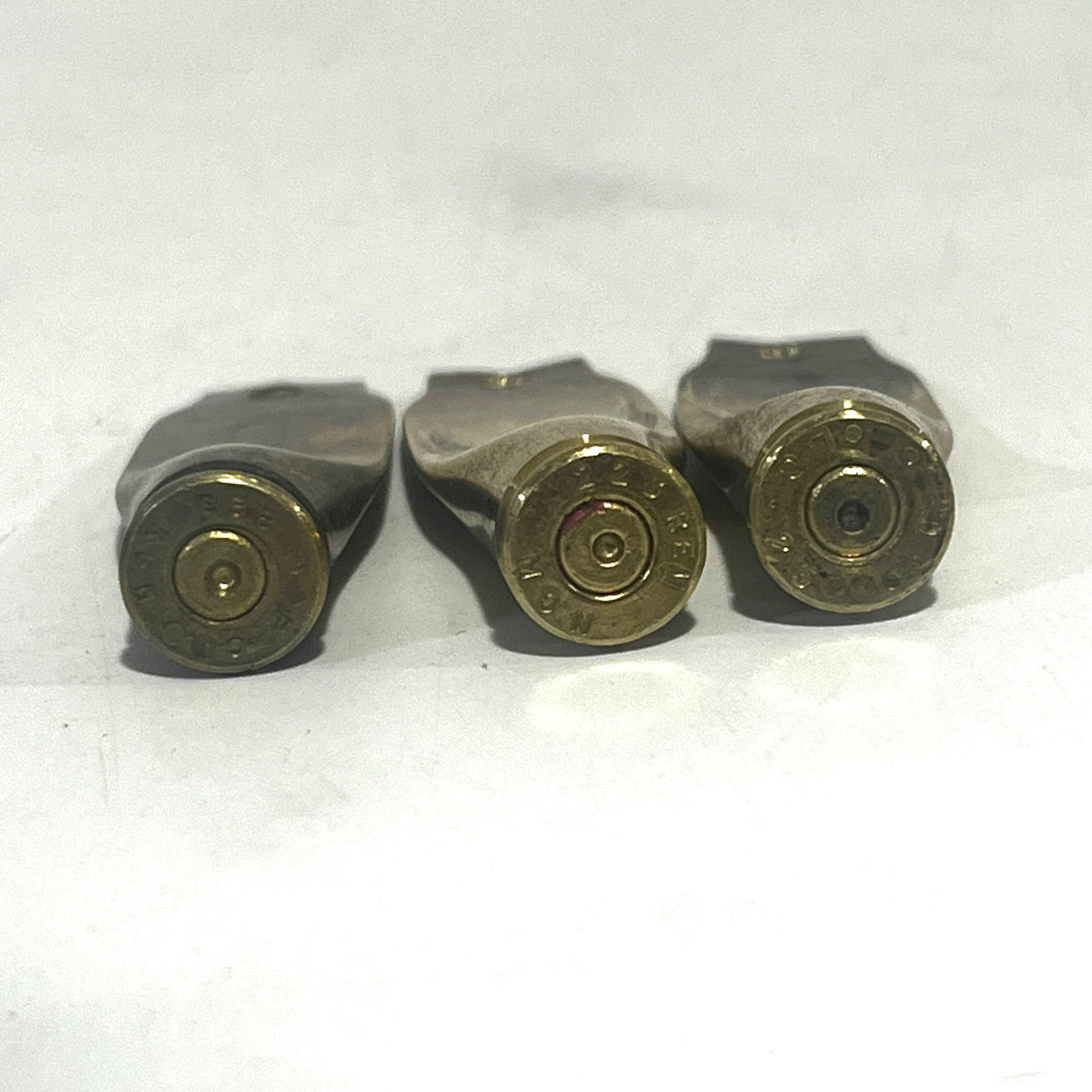 3 flattened brass casings viewed base-first showing headstamps on a white background