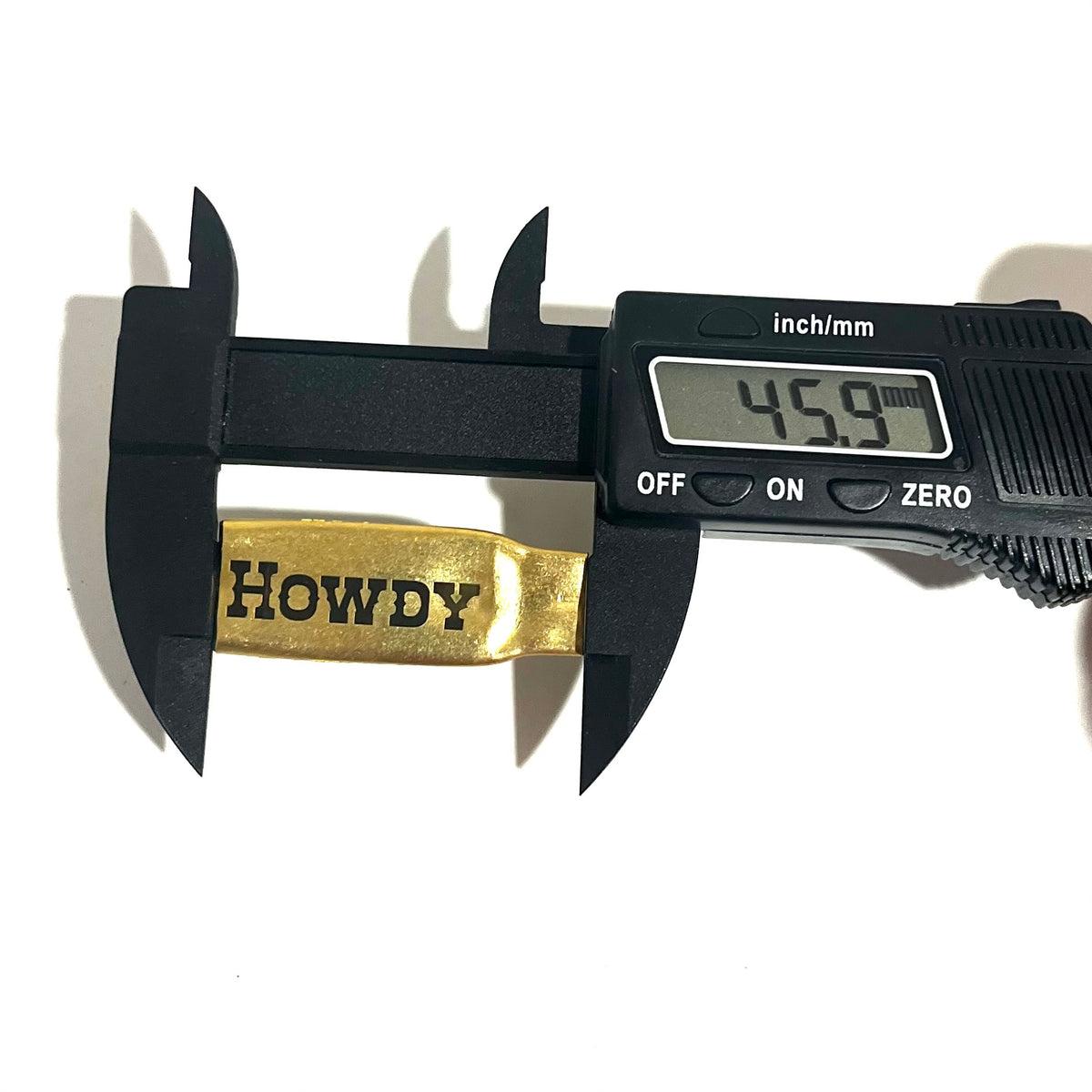 Digital caliper measuring the length of a flattened brass .308 casing engraved with the word HOWDY at 45.9 mm