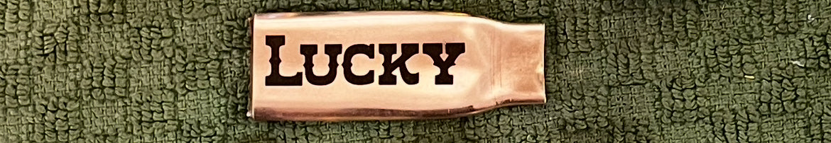 Flattened brass .308 casing engraved with the word LUCKY, laid on a green textured cloth