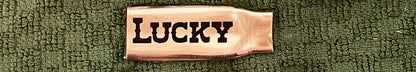 Flattened brass .308 casing engraved with the word LUCKY, laid on a green textured cloth