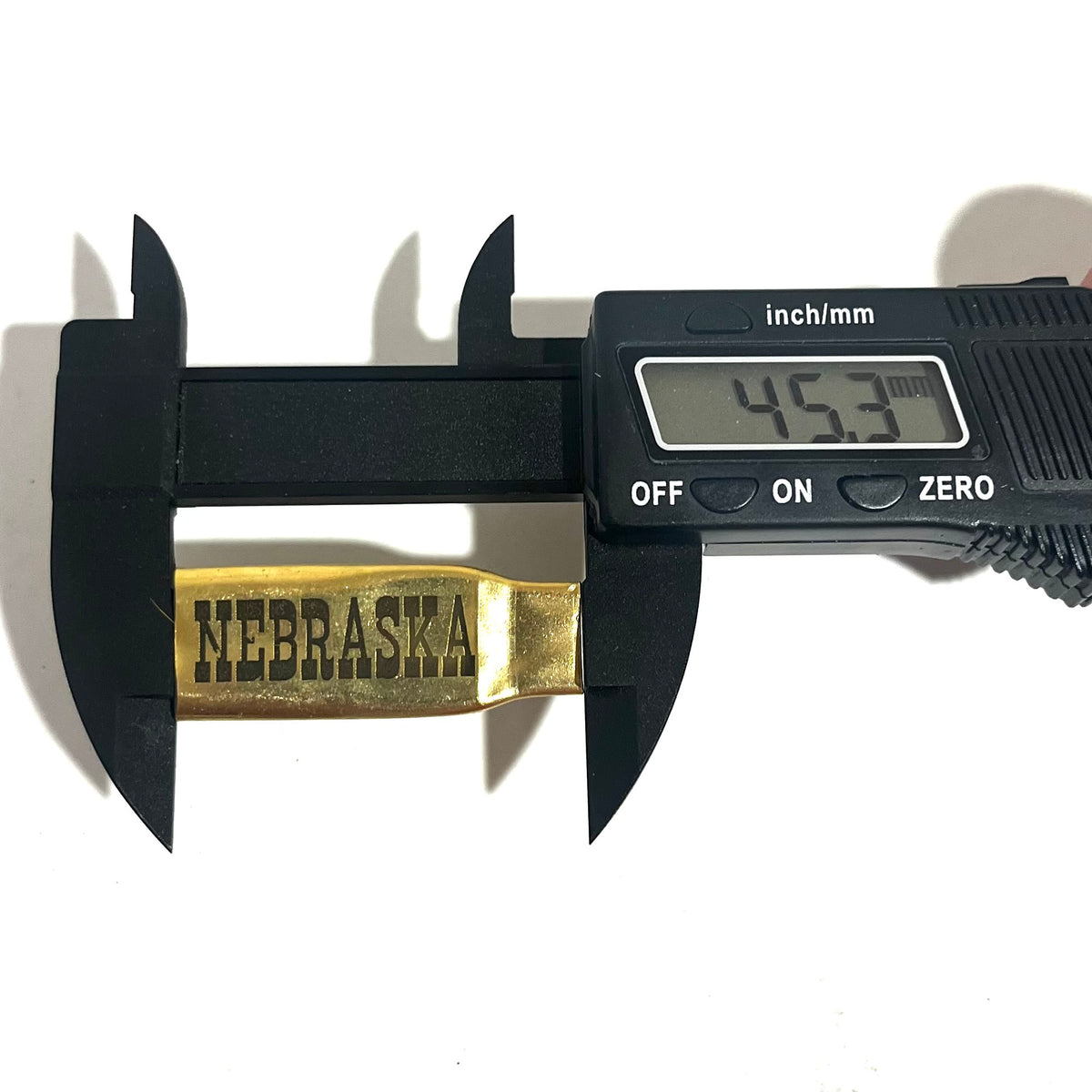 Digital caliper measuring the length of a flattened brass .308 casing engraved with the word NEBRASKA at 45.3 mm