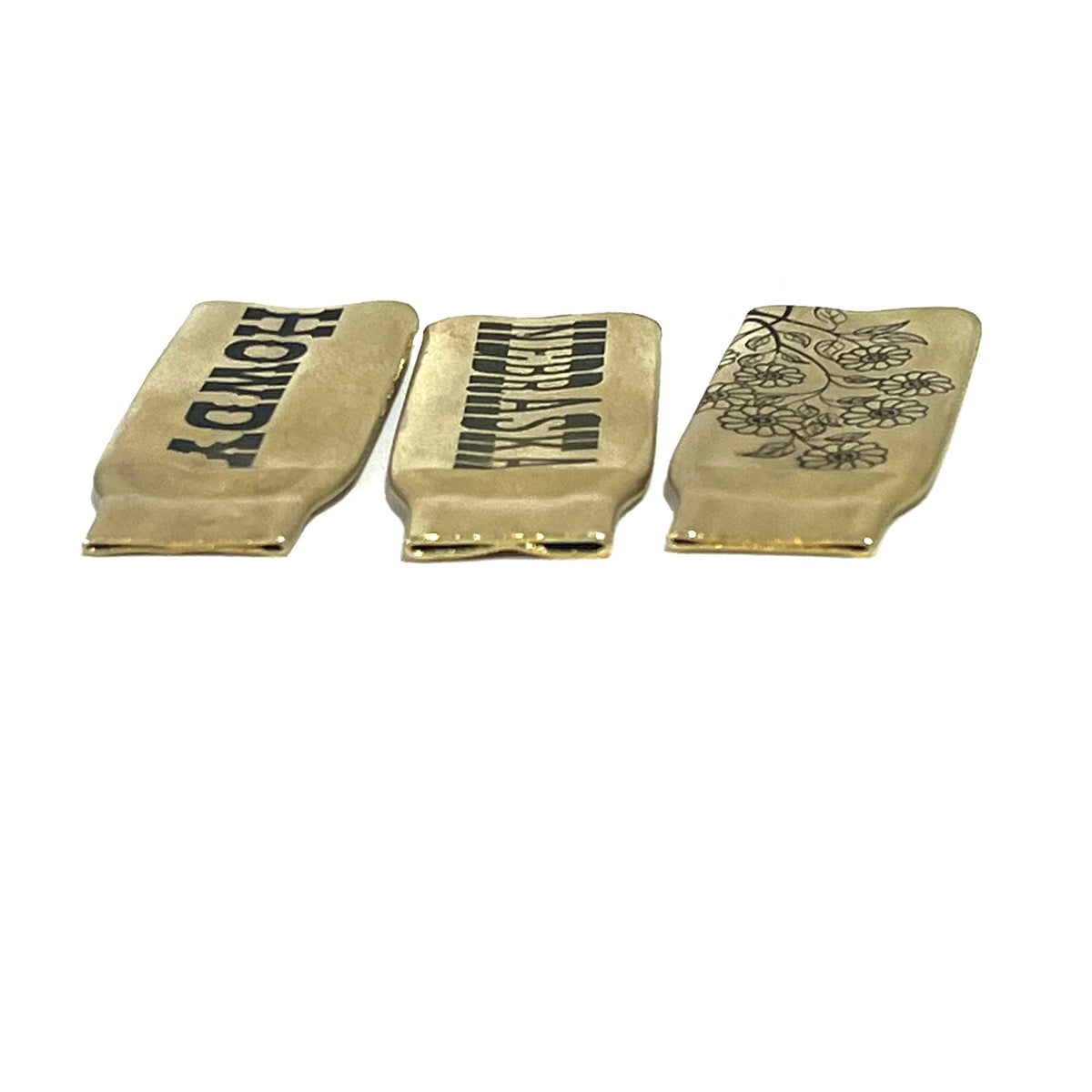 3 flattened brass .308 casings engraved with different designs reading HOWDY, NEBRASKA, and a floral branch pattern