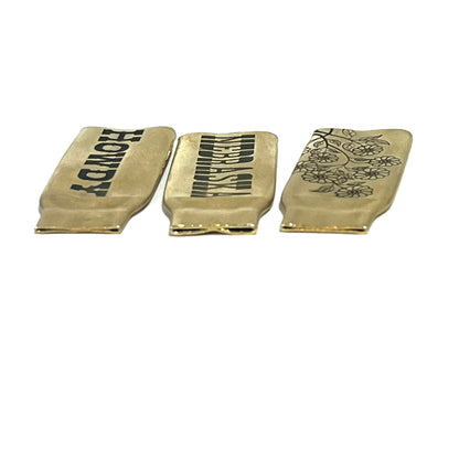 3 flattened brass .308 casings engraved with different designs reading HOWDY, NEBRASKA, and a floral branch pattern