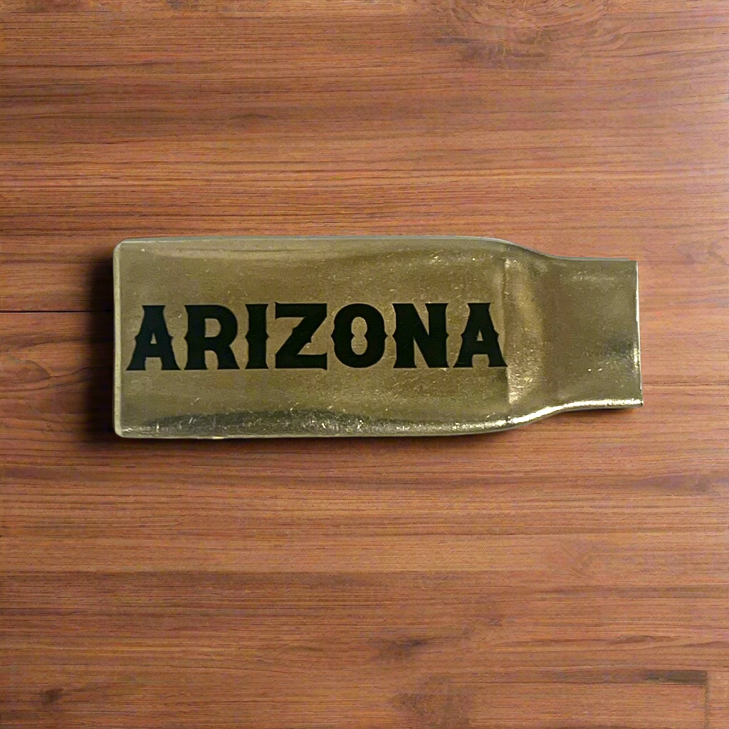 Flattened brass .308 casing engraved with Arizona in black lettering on a wood surface