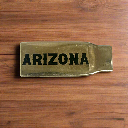 Flattened brass .308 casing engraved with Arizona in black lettering on a wood surface