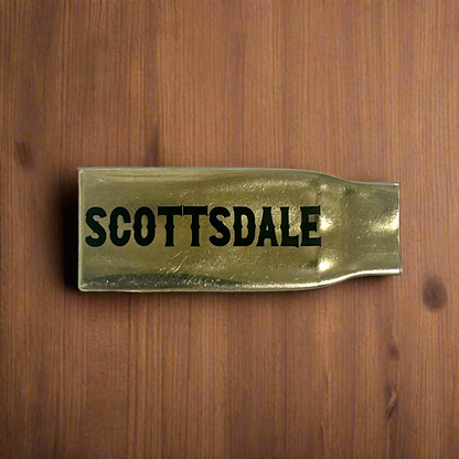 Flattened brass .308 casing engraved with Scottsdale in black lettering on a wood surface