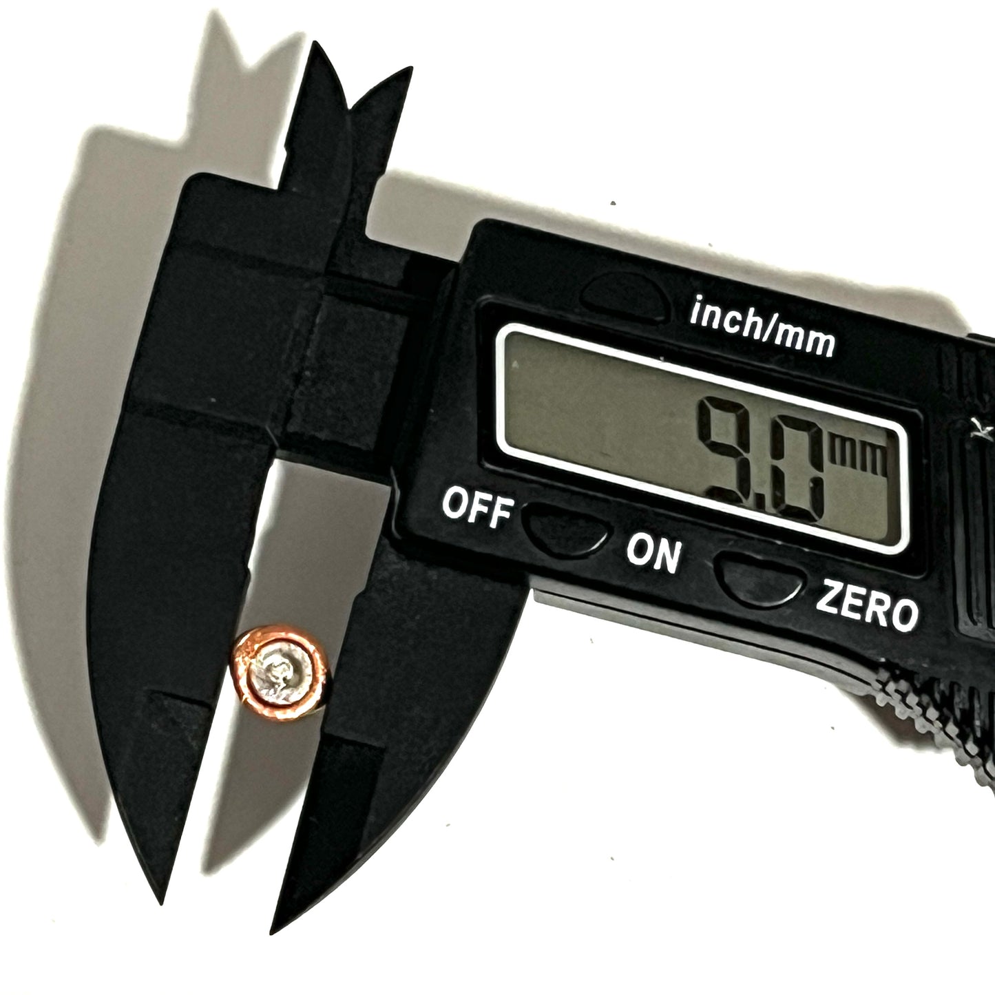 Black digital caliper measuring a single two-tone copper and silver flattened primer reading 9.0 mm.