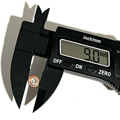 Black digital caliper measuring a single two-tone copper and silver flattened primer reading 9.0 mm.