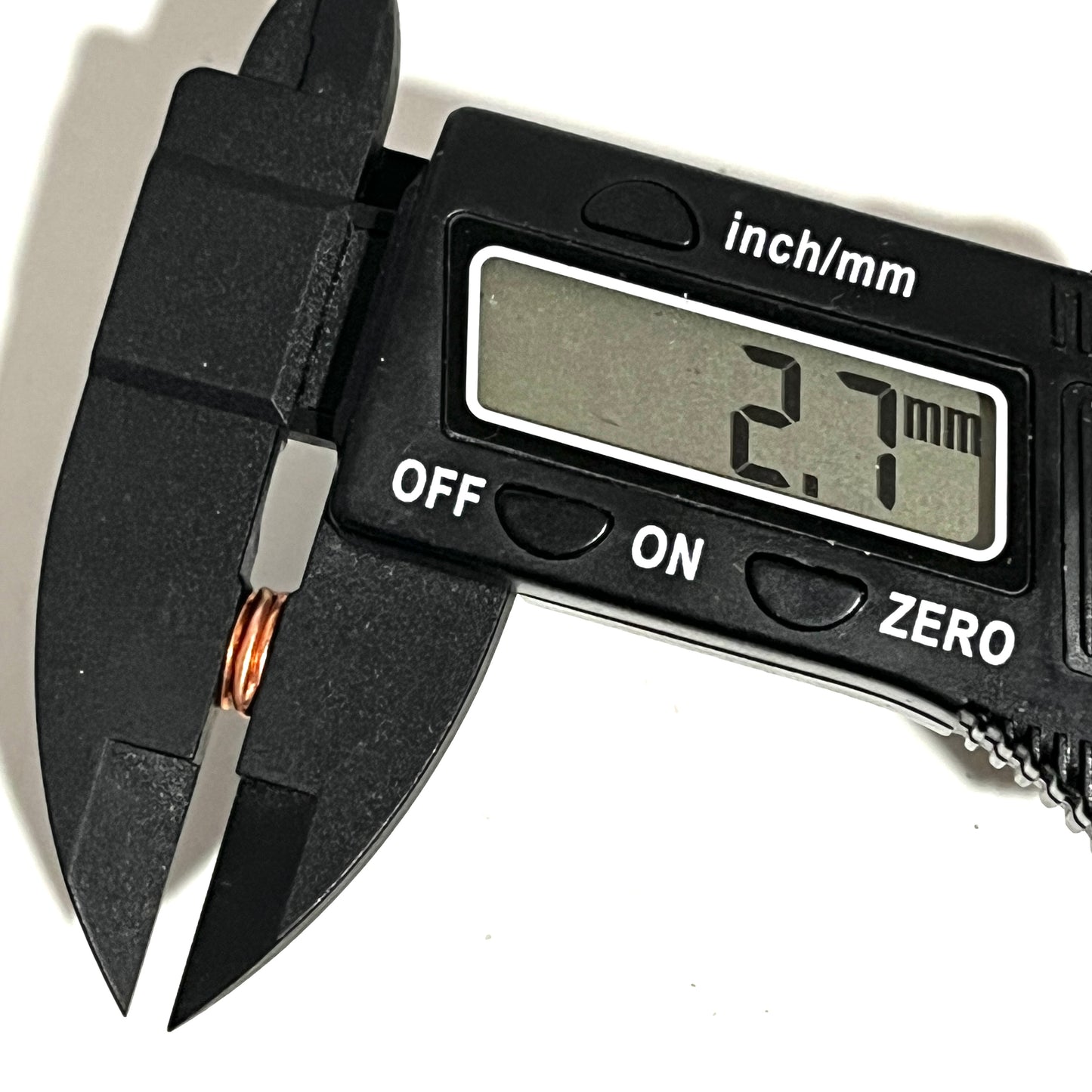 Black digital caliper measuring the 2.7 mm thickness of a copper and silver flattened primer.