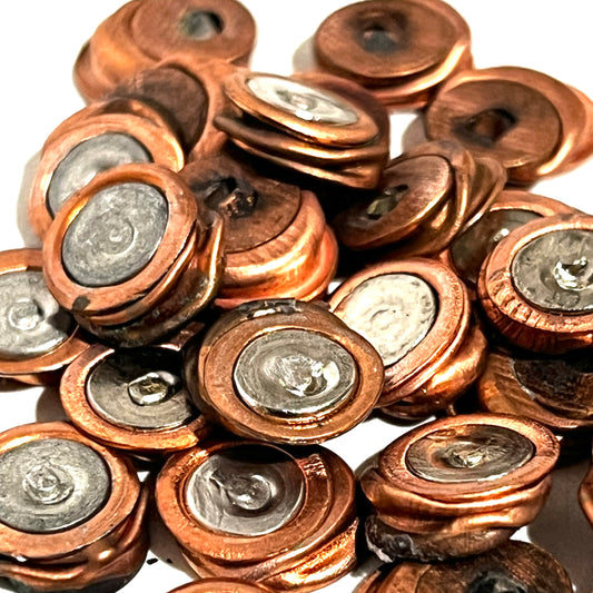 Flattened primers piled together, displaying copper and silver two-tone metallic surfaces.