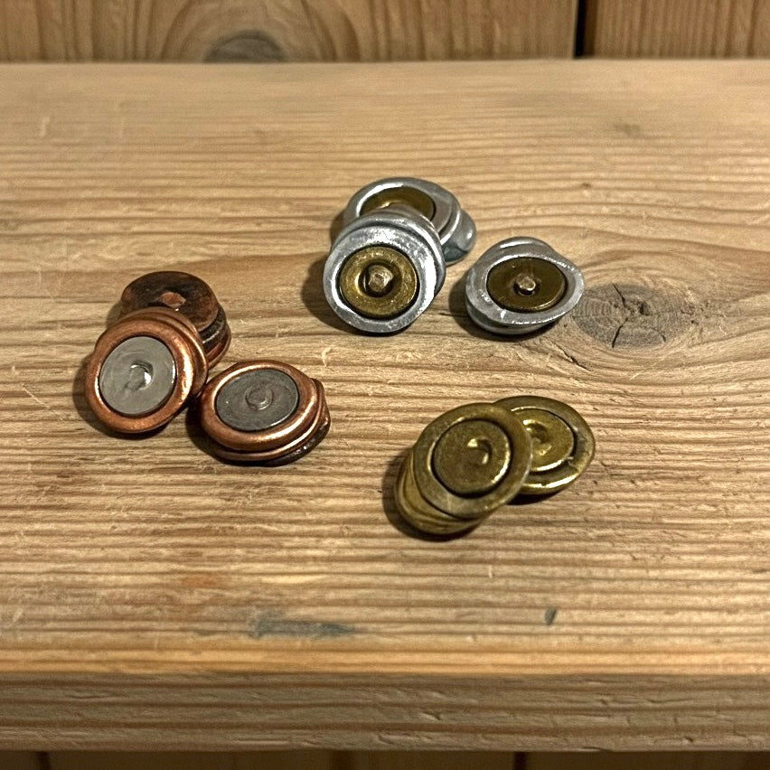 Three distinct groupings of flattened inert primers in copper, brass, and silver finishes resting on a light wooden surface.