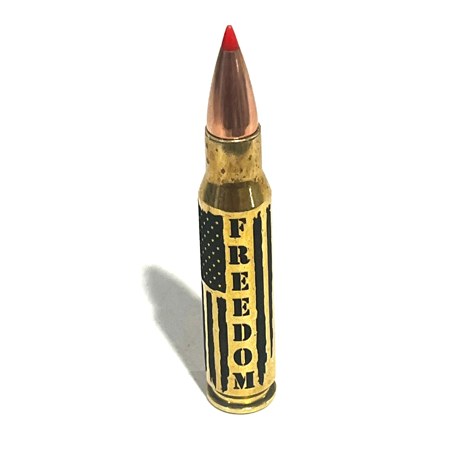 Brass .308 cartridge with red tip standing upright in close-up, engraved with 'FREEDOM' lettering and flag stripes