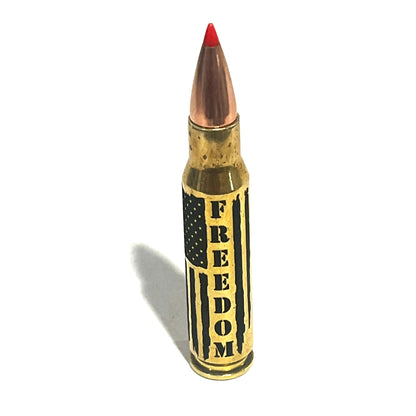 Brass .308 cartridge with red tip standing upright in close-up, engraved with 'FREEDOM' lettering and flag stripes