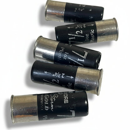 Five black fake shotgun hulls lying on their sides showing printed shot-size markings (2 3/4 inch, 1 oz, No. 7 1/2) for movie props