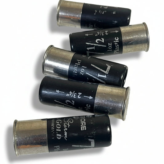 Five black fake shotgun hulls lying on their sides showing printed shot-size markings (2 3/4 inch, 1 oz, No. 7 1/2) for movie props