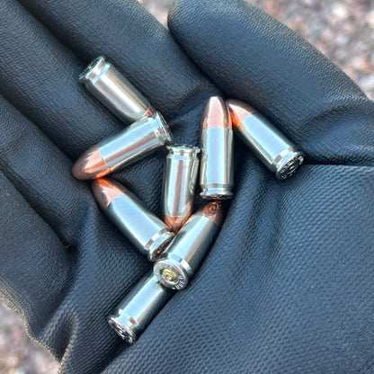Several authentic 9mm nickel dummy rounds resting in the palm of a black-gloved hand.