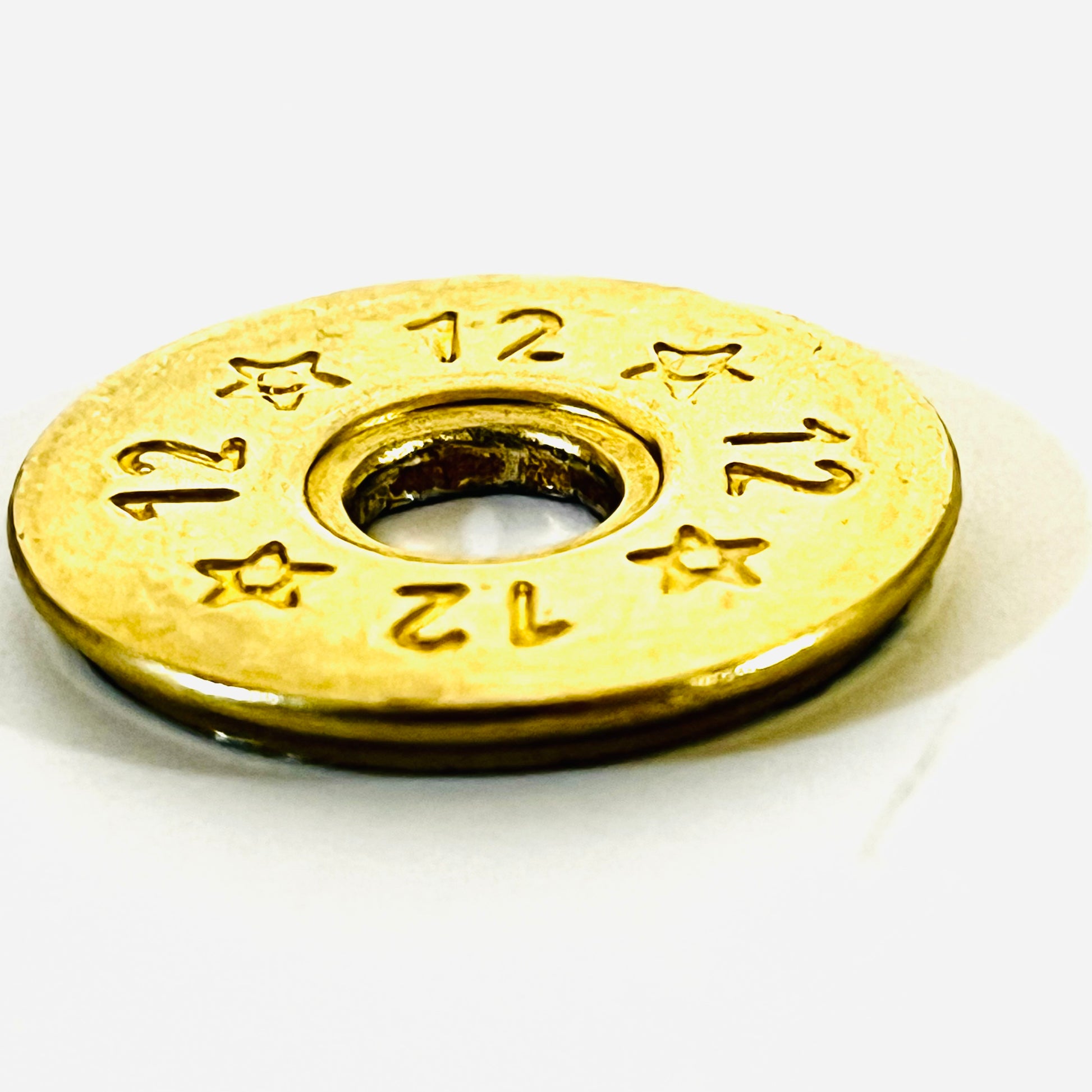 Close-up of a single deprimed 12 gauge brass shotgun shell slice with 12 and star stamped design, angled to show its edge