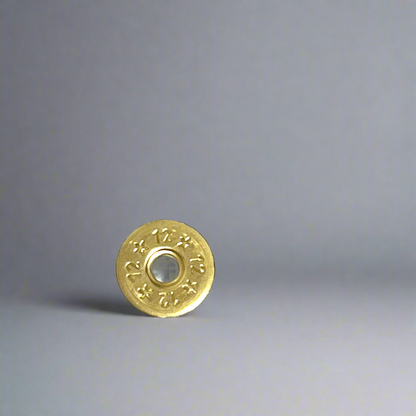 Single deprimed 12 gauge brass shotgun shell slice with 12 and star stamped design standing on a gray background