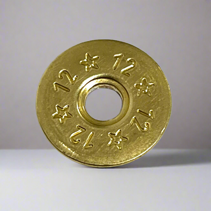 Single deprimed 12 gauge brass shotgun shell slice with 12 and star stamped design standing upright on a gray surface