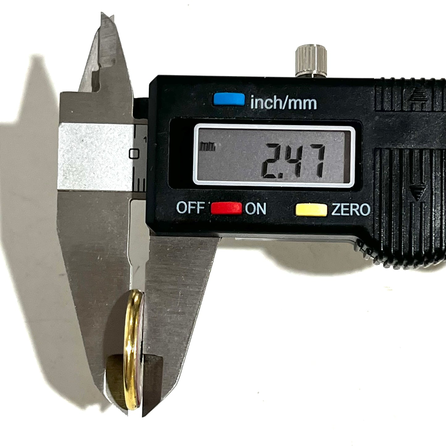 Digital caliper measuring a gold shotgun shell slice at 2.47 mm thick