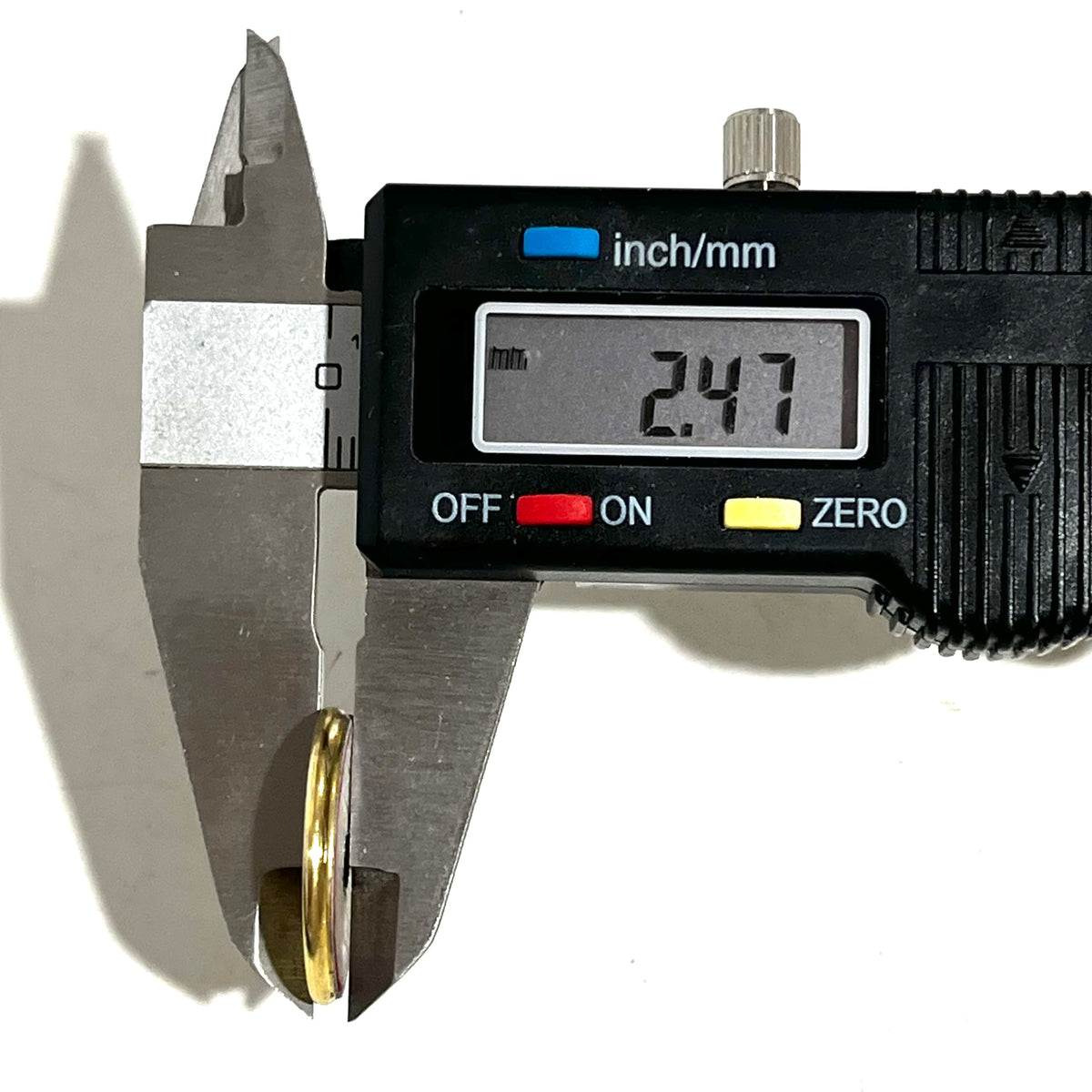 Digital caliper measuring a gold shotgun shell slice at 2.47 mm thick