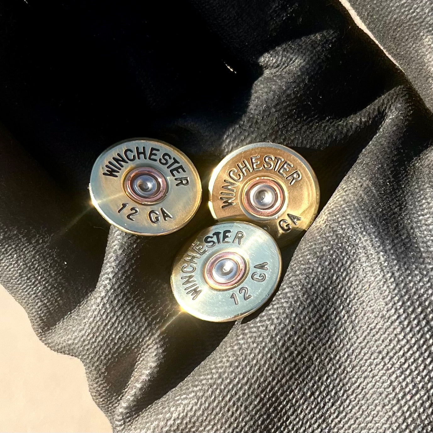 3 gold Winchester 12 GA shotgun shell slices on a dark fabric background