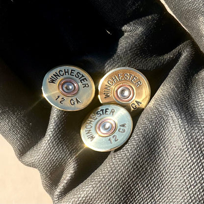 3 gold Winchester 12 GA shotgun shell slices on a dark fabric background