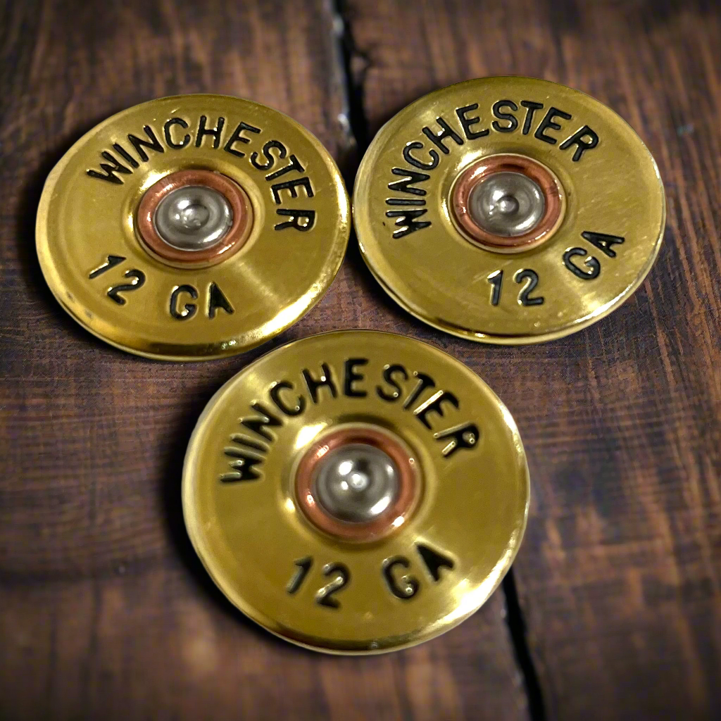 3 gold Winchester 12 GA shotgun shell slices with black lettering on a wood surface