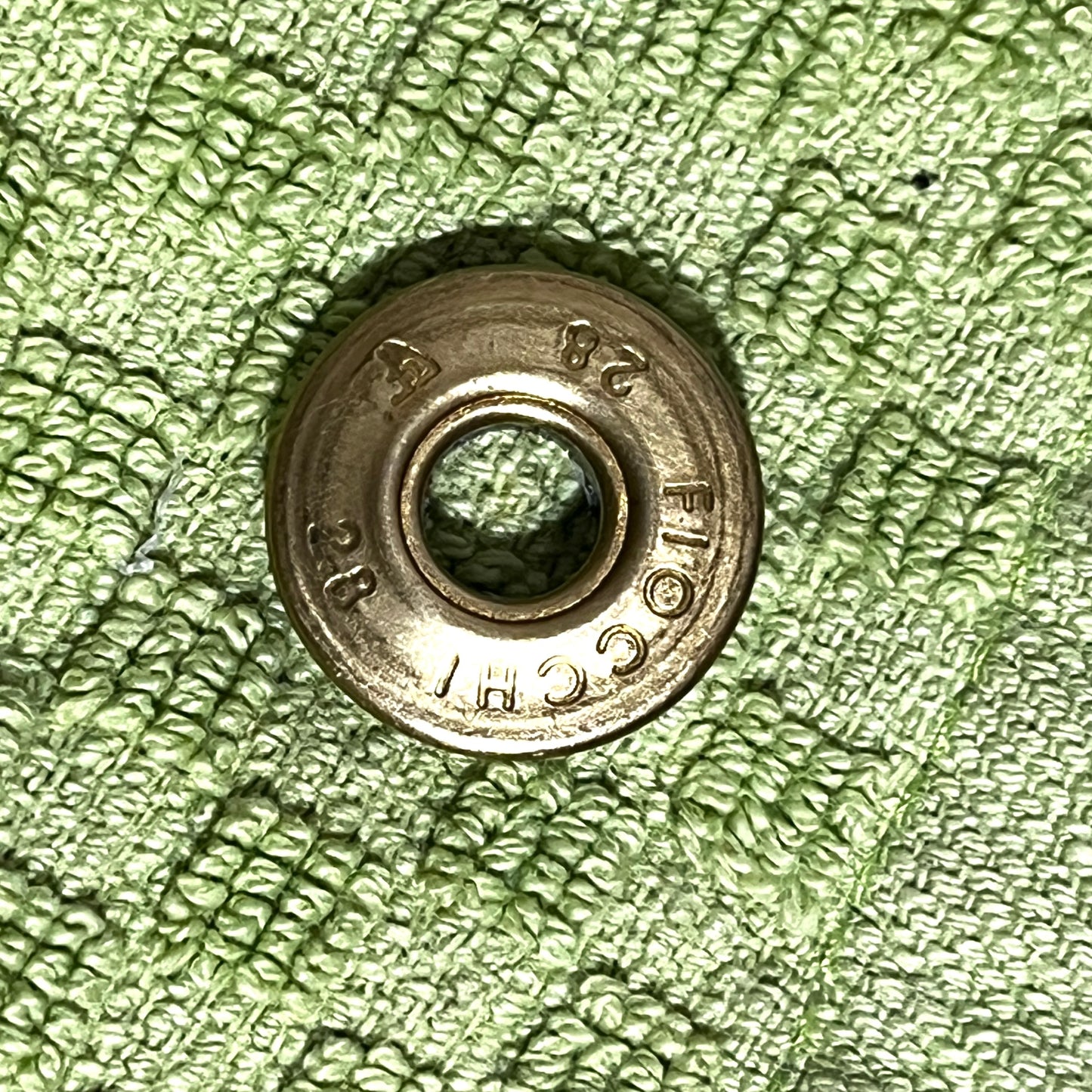 Close-up of a gold brass Fiocchi 28 gauge shotgun shell slice on a green cloth background