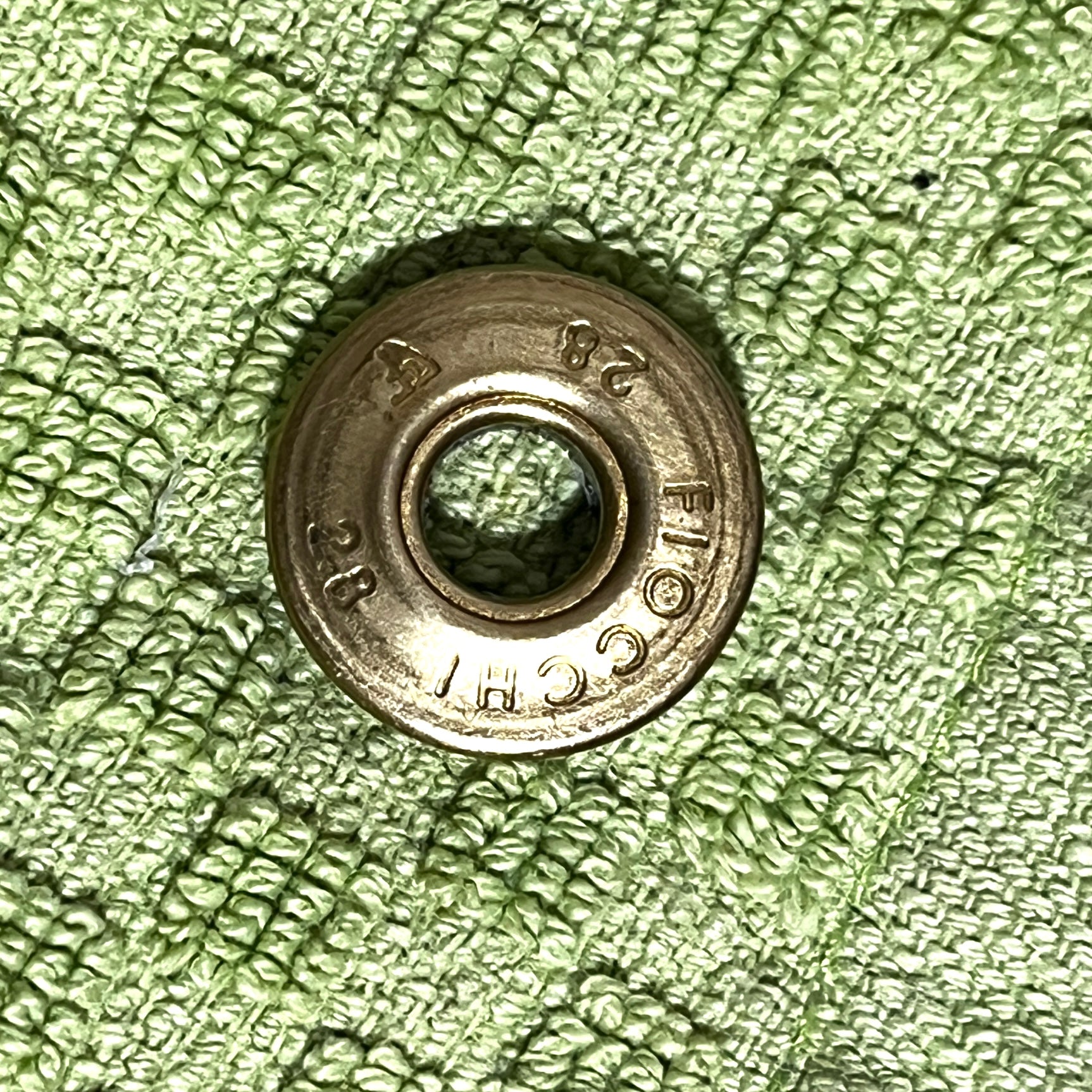Close-up of a gold brass Fiocchi 28 gauge shotgun shell slice on a green cloth background