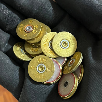 A gloved hand holding a pile of gold Winchester 12 gauge shotgun shell slices with red and cream centers