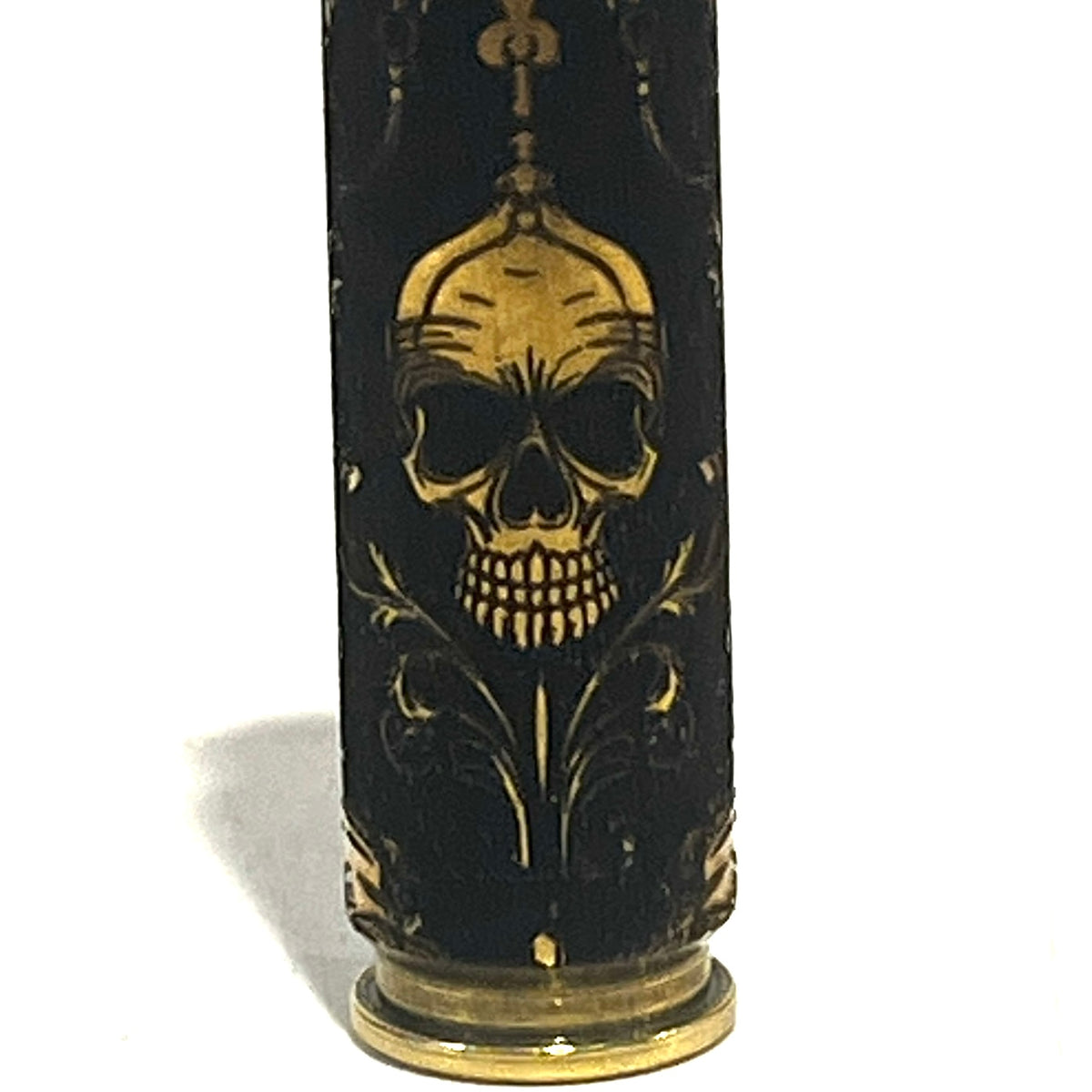 Close-up of a brass rifle casing engraved with a gold gothic skull wearing a crown and scrollwork design