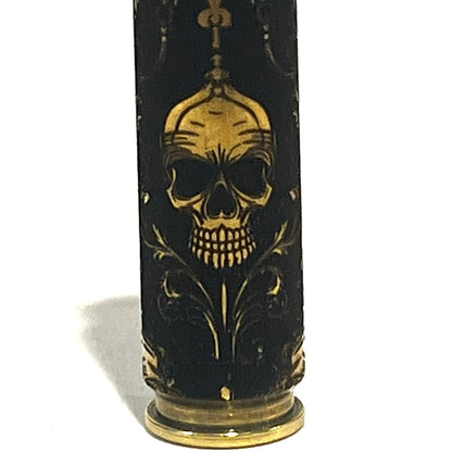 Close-up of a brass rifle casing engraved with a gold gothic skull wearing a crown and scrollwork design